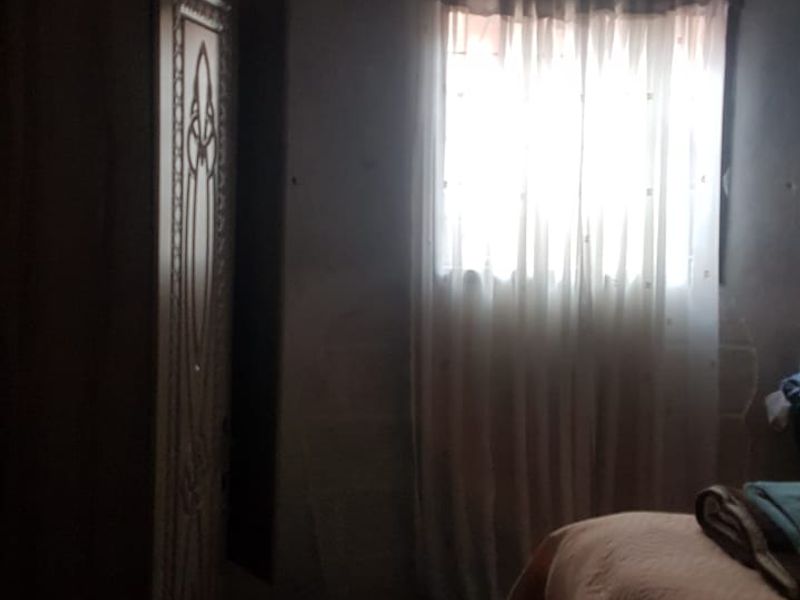A dimly lit bedroom space featuring a window with curtains and basic wall finishes, requiring renovation to improve brightness and overall condition.
