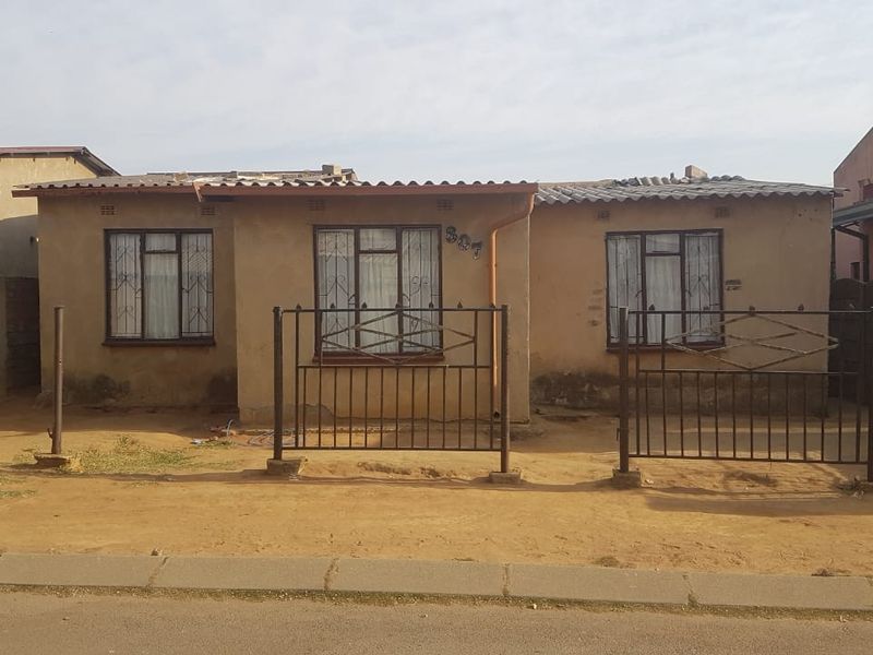 Front elevation of a single-story house featuring metal security gates, burglar bars, and a corrugated roof, requiring exterior maintenance and landscaping.