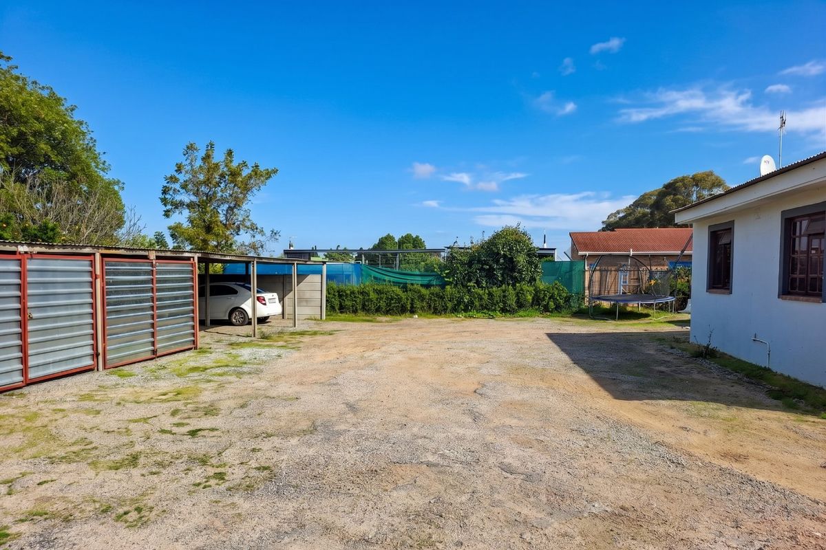Rear exterior view showing a gravel driveway, a metal carport structure, and a storage shed area with perimeter fencing.