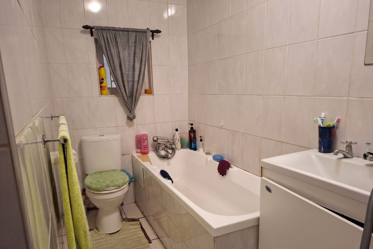 A functional bathroom featuring a bathtub, toilet, and vanity basin with full-height wall tiling.