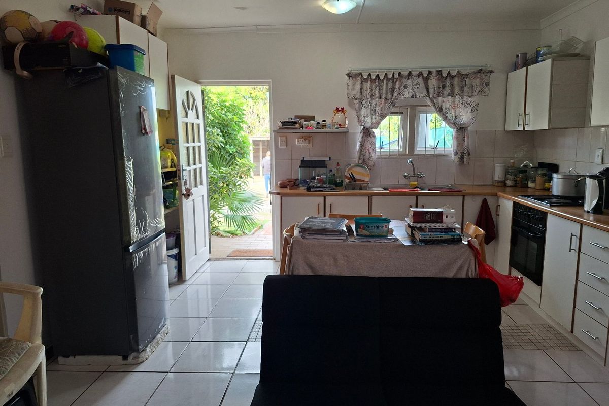 A functional kitchen featuring tiled flooring, built-in cabinetry, and a direct access point to the rear garden area.