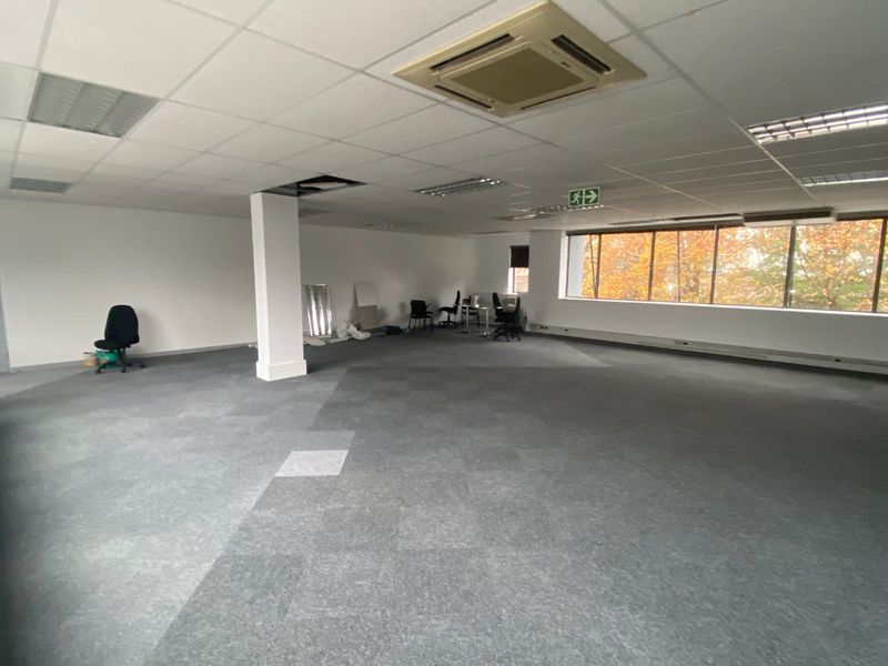 Open-plan commercial office space featuring suspended ceilings, recessed lighting, ducted air conditioning, and large windows providing natural light.