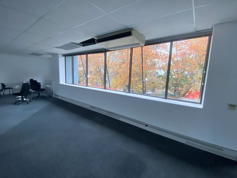 A bright, open-plan office space featuring large windows, suspended ceilings, and integrated air conditioning, offering a functional workspace with pleasant exterior views.