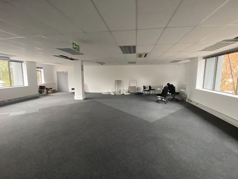 Spacious open-plan commercial office area featuring suspended ceilings, recessed lighting, and large windows providing natural light.