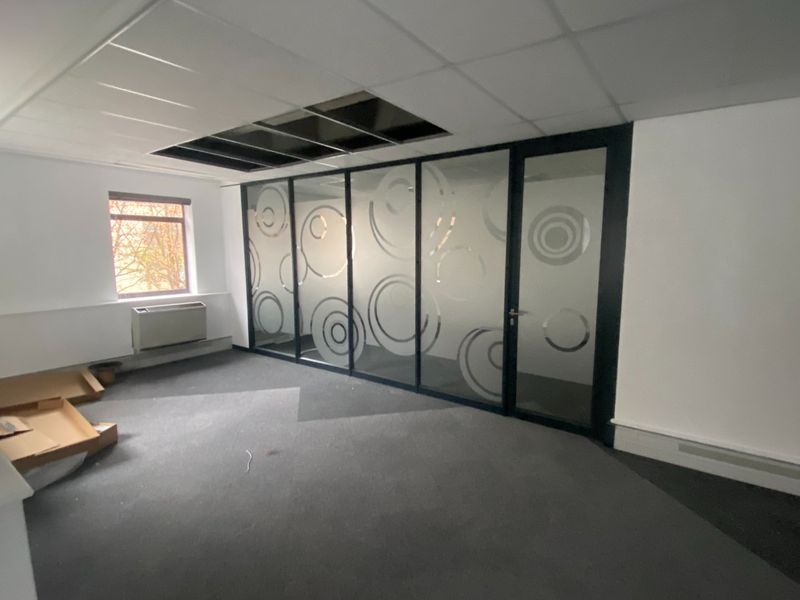 Empty office space featuring a glass partition wall, carpeted flooring, and a suspended ceiling with missing tiles requiring repair.