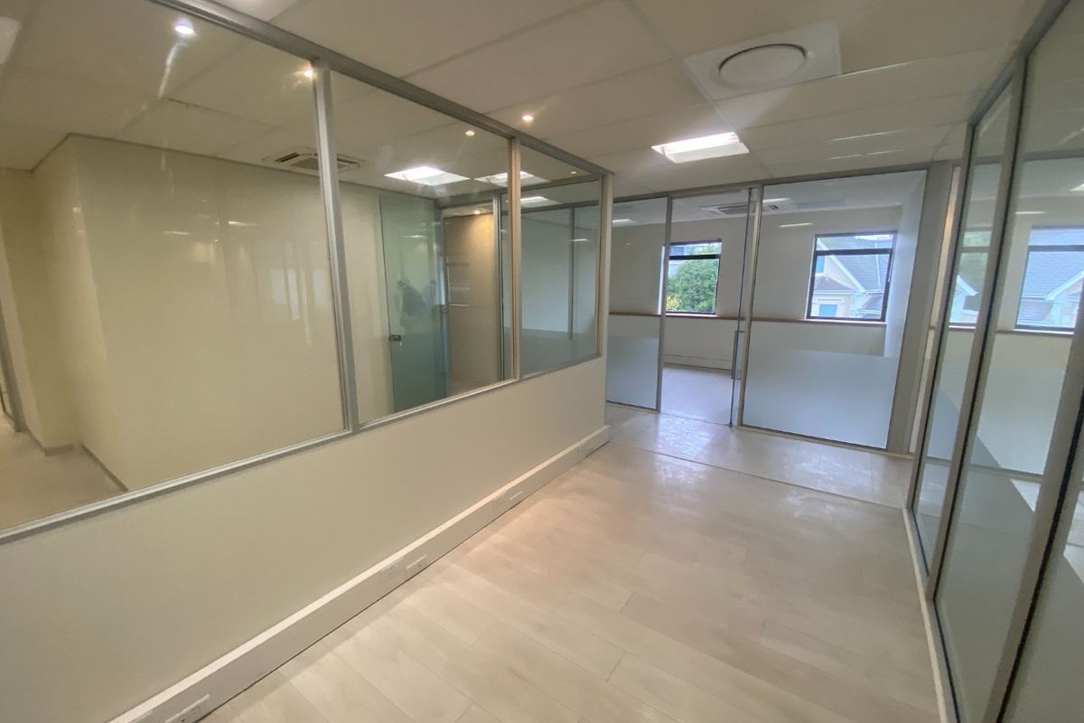 Modern commercial office space featuring glass partitioning, suspended ceilings, and light laminate flooring, offering a bright and professional work environment.