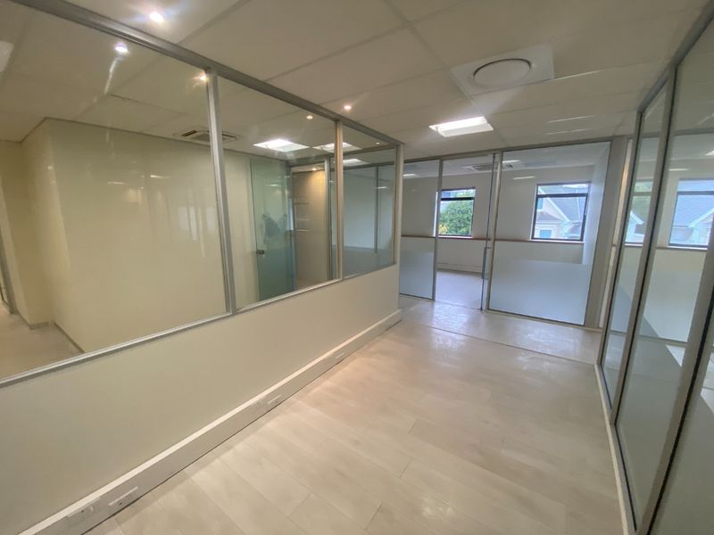 Modern commercial office space featuring glass partitioning, suspended ceilings, and light laminate flooring, offering a bright and professional work environment.