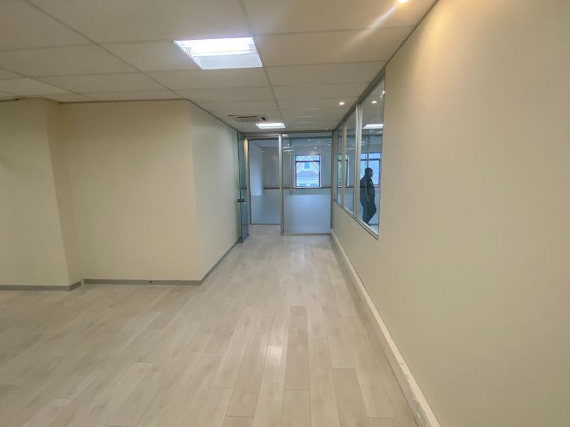 A bright, empty commercial office space featuring modern laminate flooring, suspended ceilings, and glass partition walls providing a clean, professional environment.