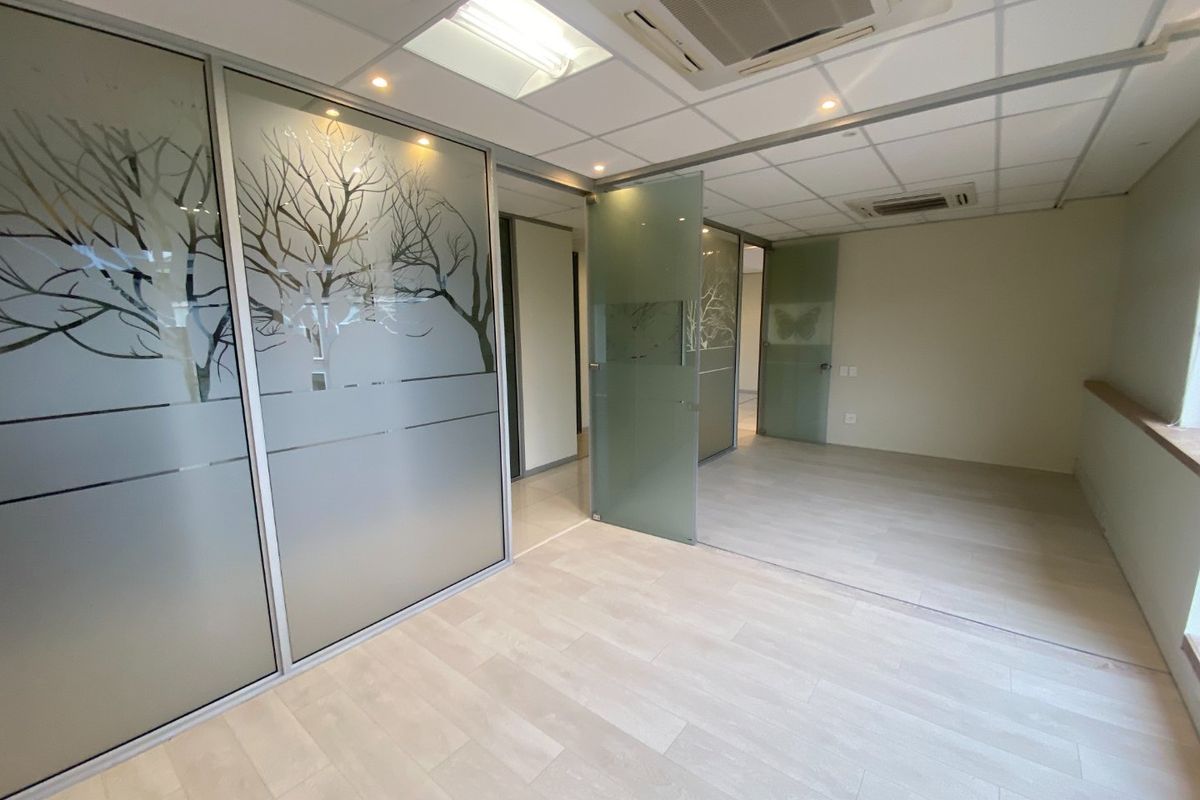 Modern commercial office space featuring frosted glass partitions, suspended ceilings with integrated air conditioning, and light-toned laminate flooring.