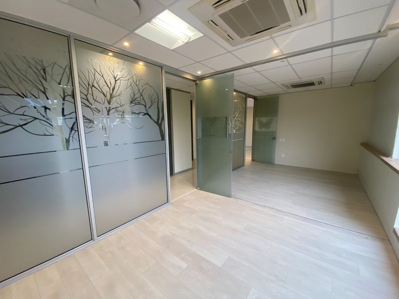 Modern commercial office space featuring frosted glass partitions, suspended ceilings with integrated air conditioning, and light-toned laminate flooring.