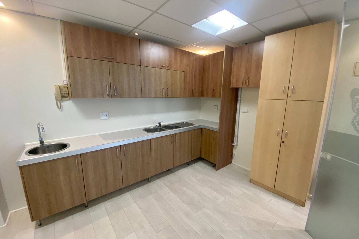 A clean and functional commercial kitchenette featuring ample laminate cabinetry, dual sink stations, and modern drop ceiling lighting.