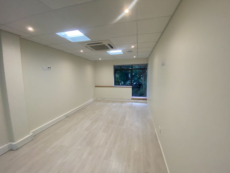 A bright, vacant office space featuring a suspended ceiling with integrated air conditioning, recessed lighting, and modern laminate flooring.