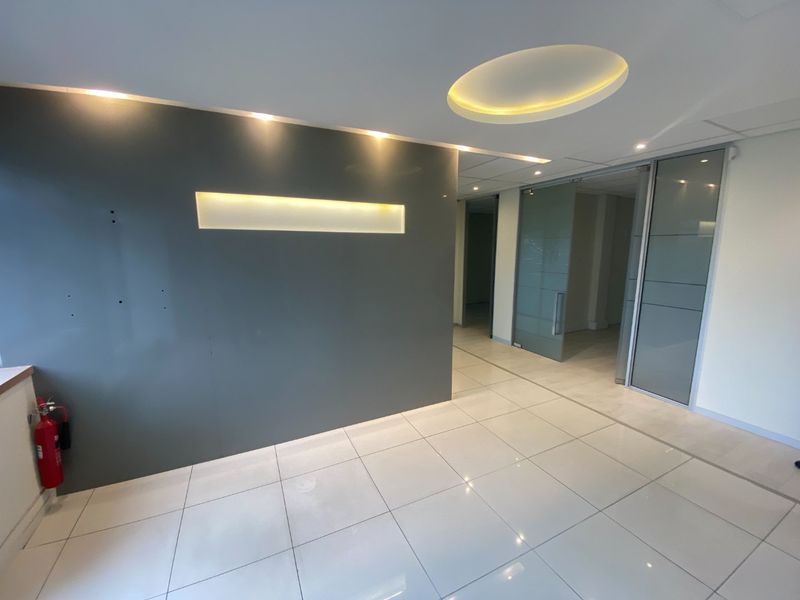 Modern commercial entrance area featuring polished tile flooring, a contemporary feature wall with recessed lighting, and glass partition doors leading to office space.