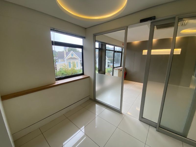 A modern, vacant office space featuring tiled flooring, recessed ceiling lighting, and glass partition walls, offering a bright and professional work environment.