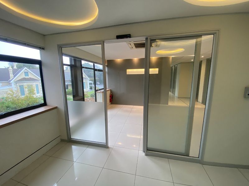 Modern commercial office space featuring tiled flooring, recessed ceiling lighting, and glass sliding doors, providing a bright and professional work environment.