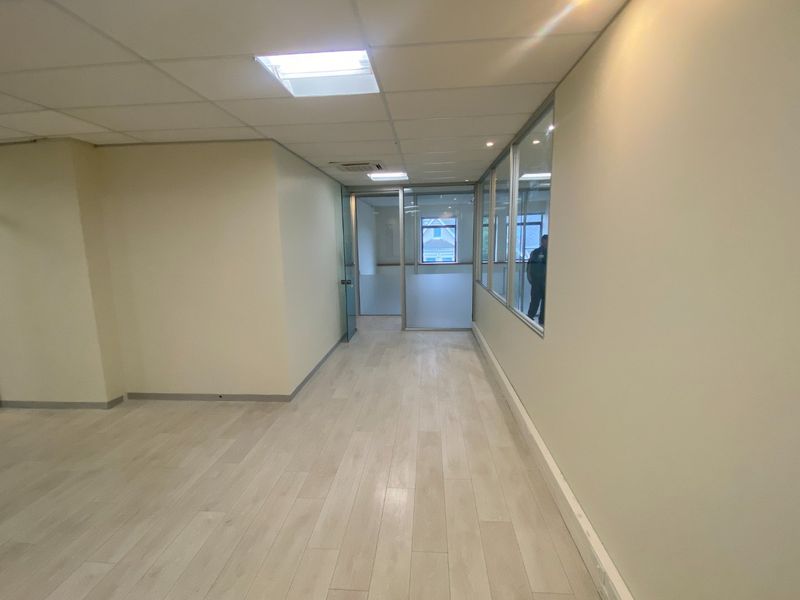 A bright, vacant commercial office space featuring modern laminate flooring, suspended ceilings with recessed lighting, and glass partition walls for a professional layout.