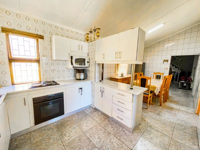 Open-plan kitchen featuring built-in oven, electric hob, and laminate cabinetry with a breakfast bar, flowing into the adjacent dining area.