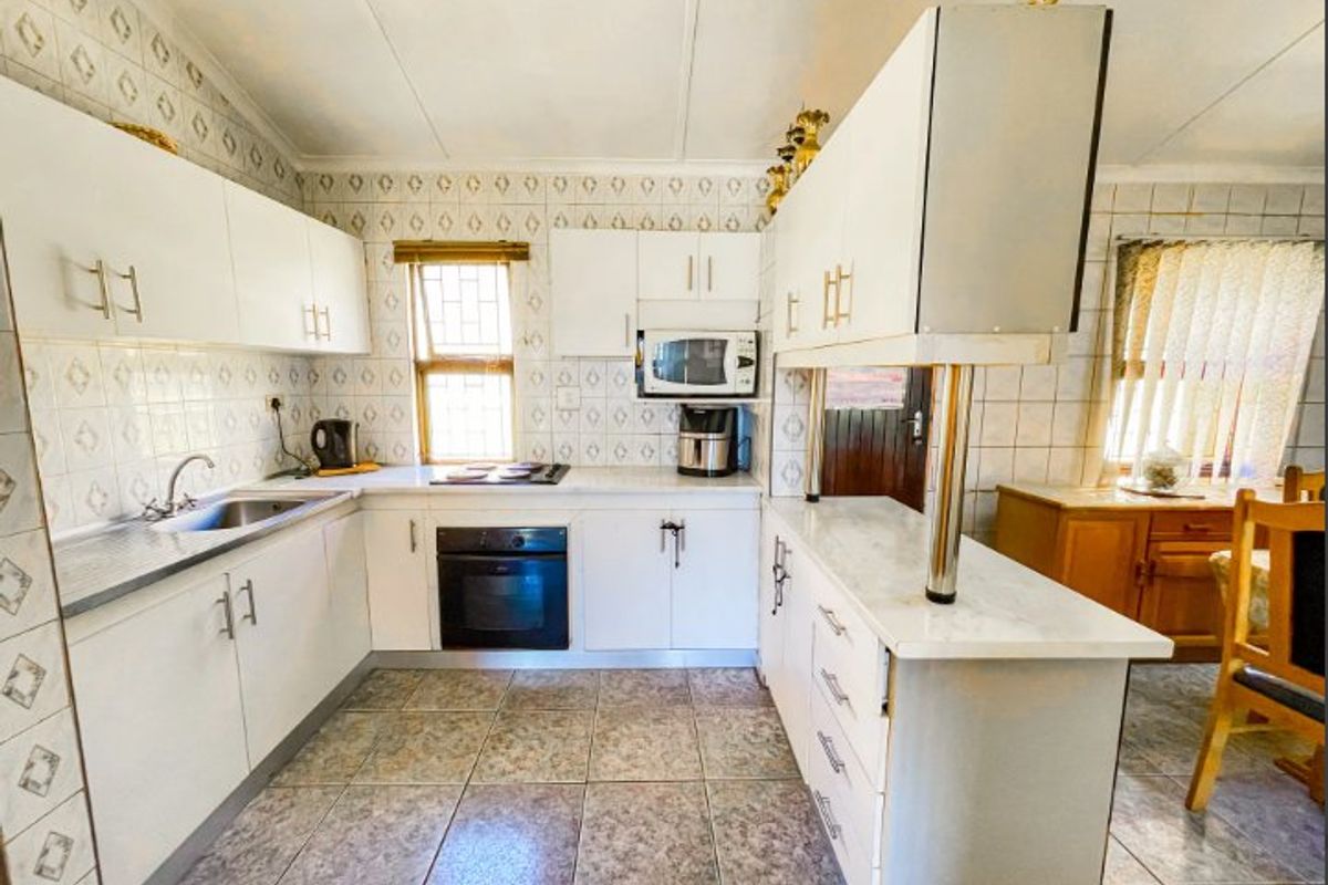 A functional kitchen featuring white built-in cabinetry, laminate countertops, integrated oven and hob, and tiled finishes throughout.