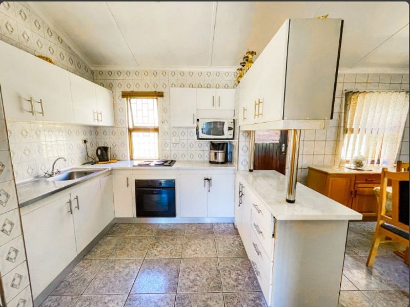 A functional kitchen featuring white built-in cabinetry, laminate countertops, integrated oven and hob, and tiled finishes throughout.