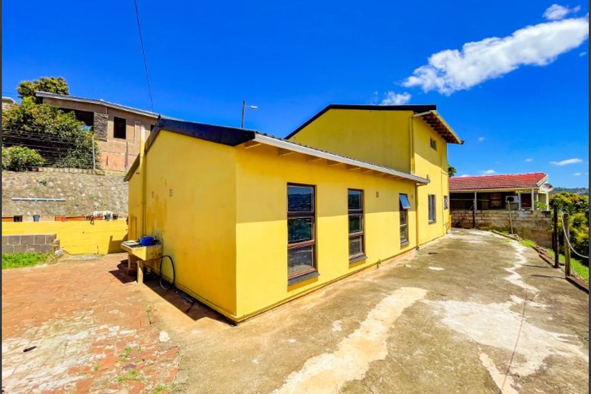Rear exterior view of the property featuring a yellow facade, concrete and brick paved yard, and an external utility sink.