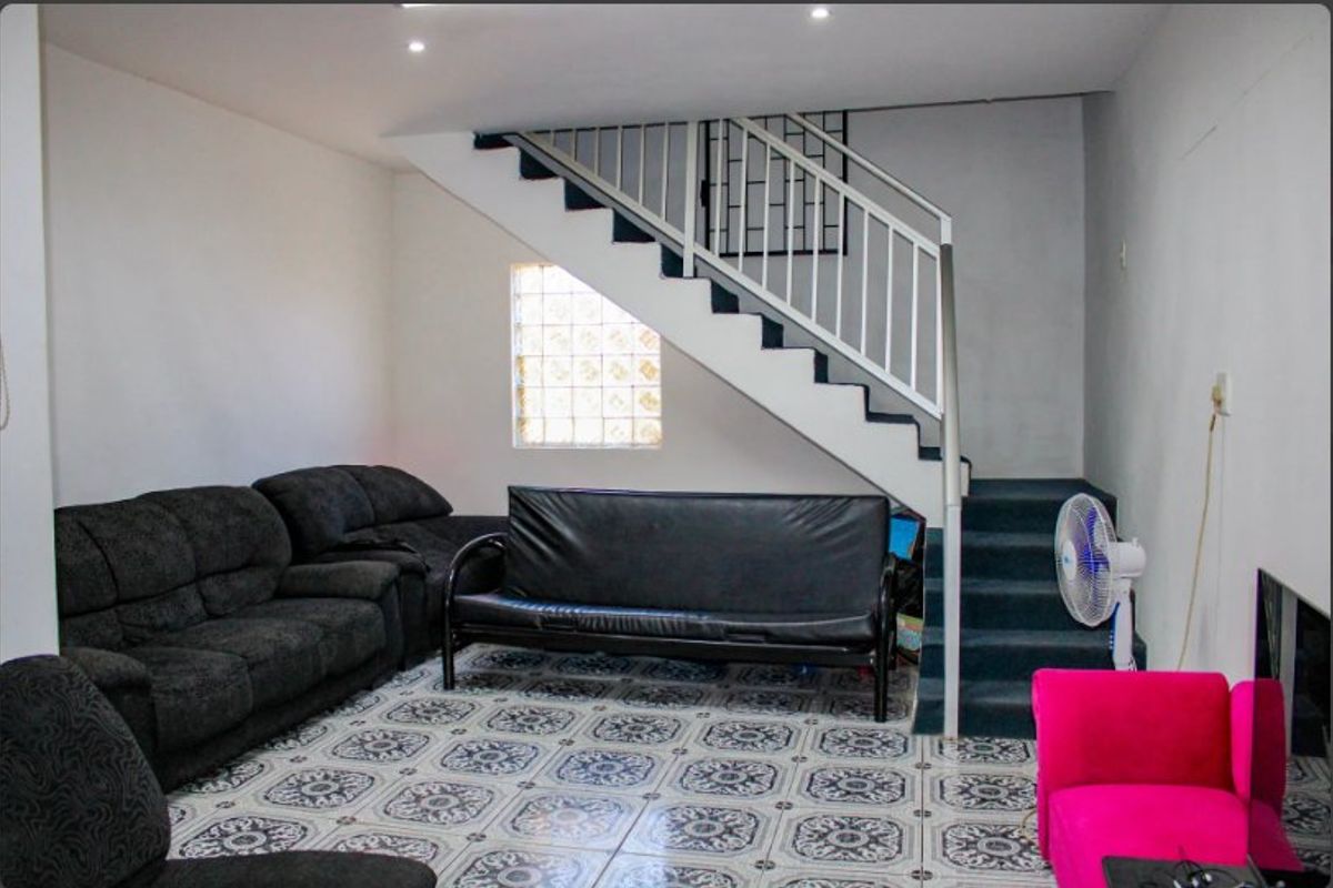 Living room featuring patterned floor tiles, a staircase with a metal railing, and a glass block window providing natural light.