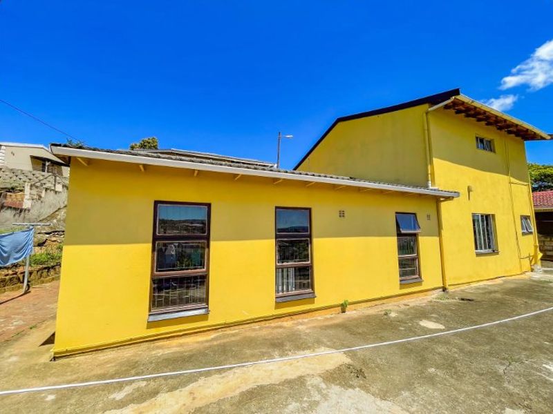 Rear view of the property featuring yellow painted exterior walls, concrete paving, and aluminium window frames with security bars.
