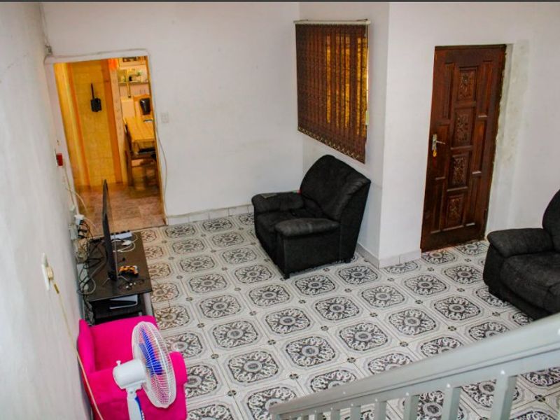 Living area featuring patterned ceramic floor tiles, a timber door, and access to an adjoining room, showing signs of wear and dated finishes.