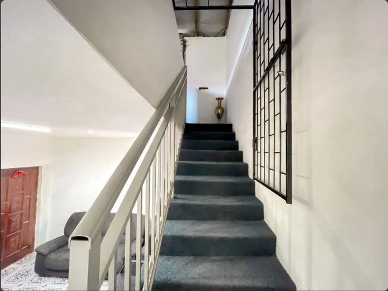 Interior staircase featuring a metal balustrade and security gate, leading to an upper level with an unfinished ceiling.