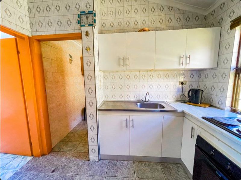 A compact kitchen featuring white cabinetry, a stainless steel sink, and dated patterned wall tiles, offering potential for a modern renovation.