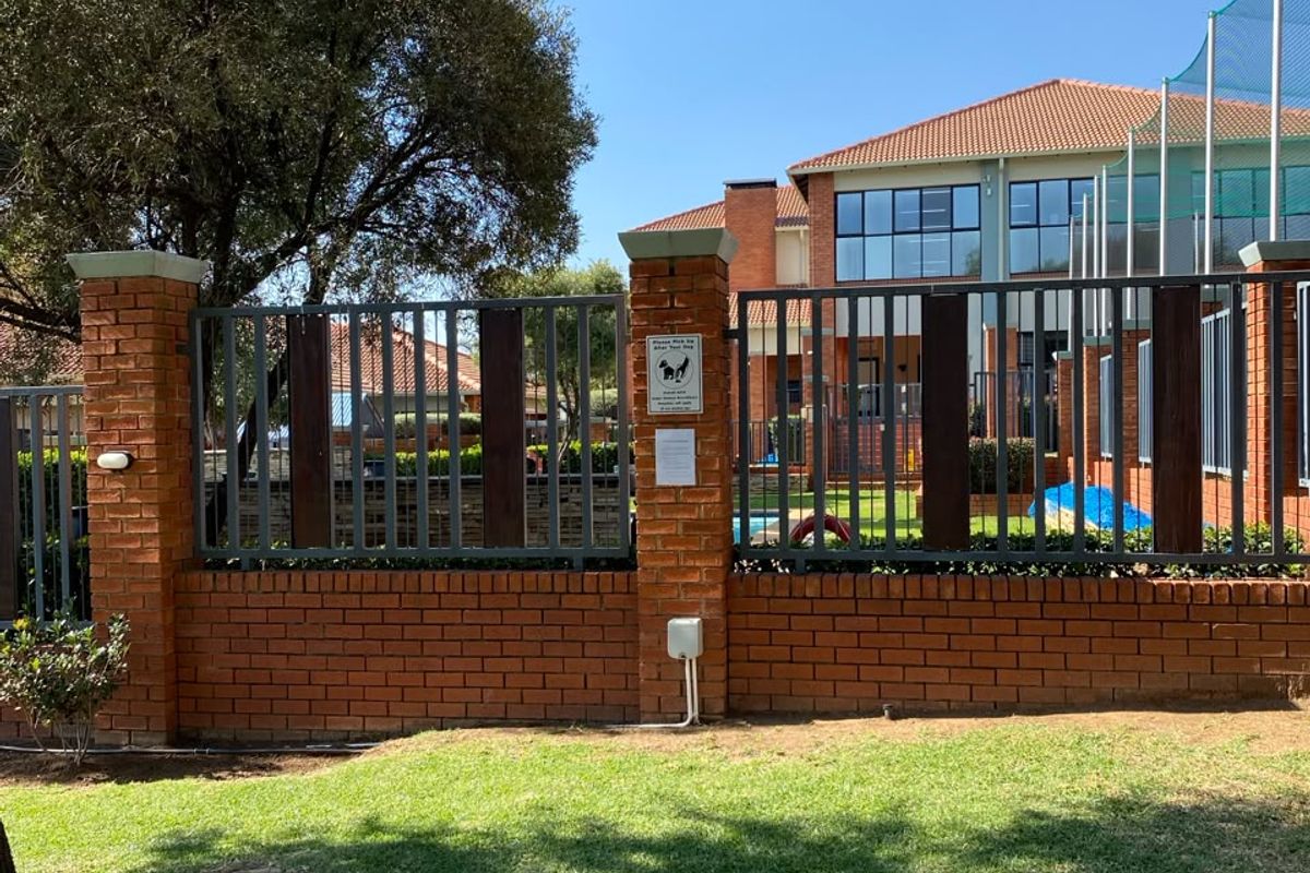 A view of the rear exterior featuring a well-maintained brick and metal boundary fence, landscaped lawn, and a multi-story building with a tiled roof.