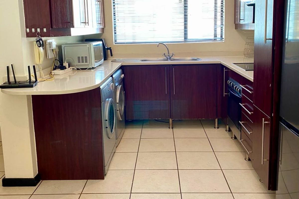 A functional kitchen featuring dark wood cabinetry, stone countertops, integrated appliances, and tiled flooring, providing a practical workspace with natural light.