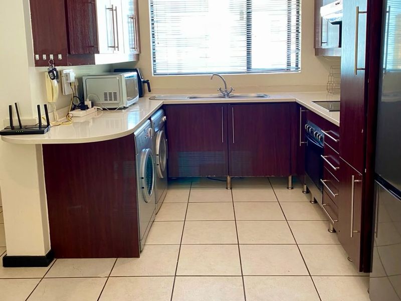 A functional kitchen featuring dark wood cabinetry, stone countertops, integrated appliances, and tiled flooring, providing a practical workspace with natural light.