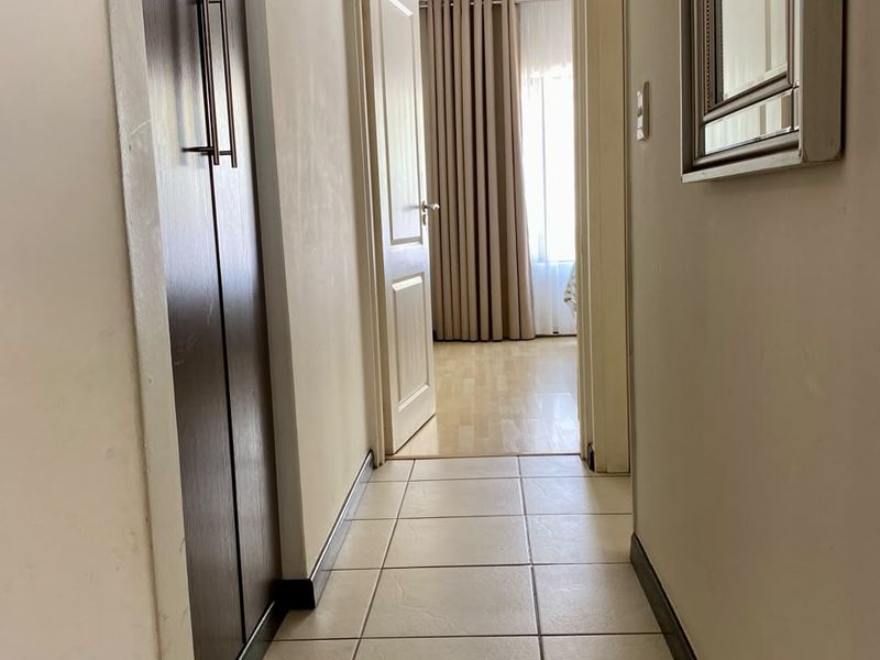 A clean, functional hallway featuring tiled flooring and a built-in storage cupboard, providing access to adjacent rooms.