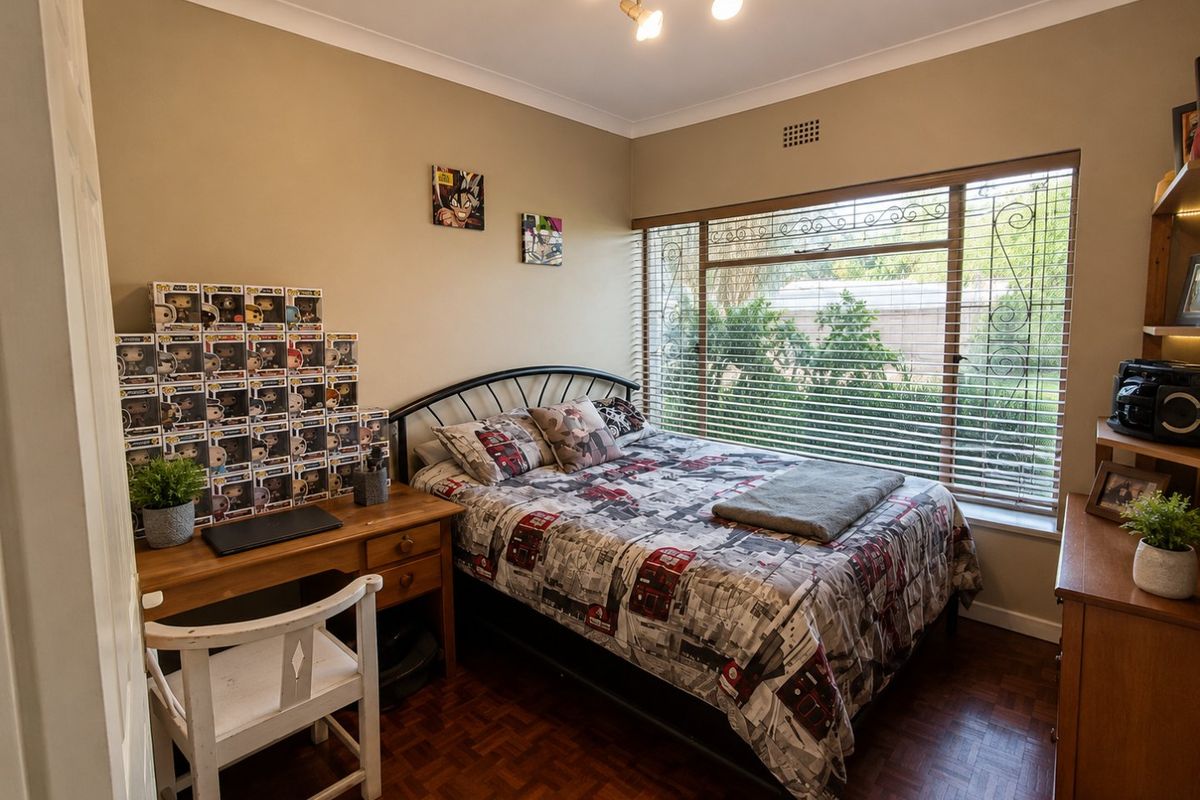 A well-lit bedroom featuring classic parquet flooring, a large window with security bars, and coved ceiling detailing.
