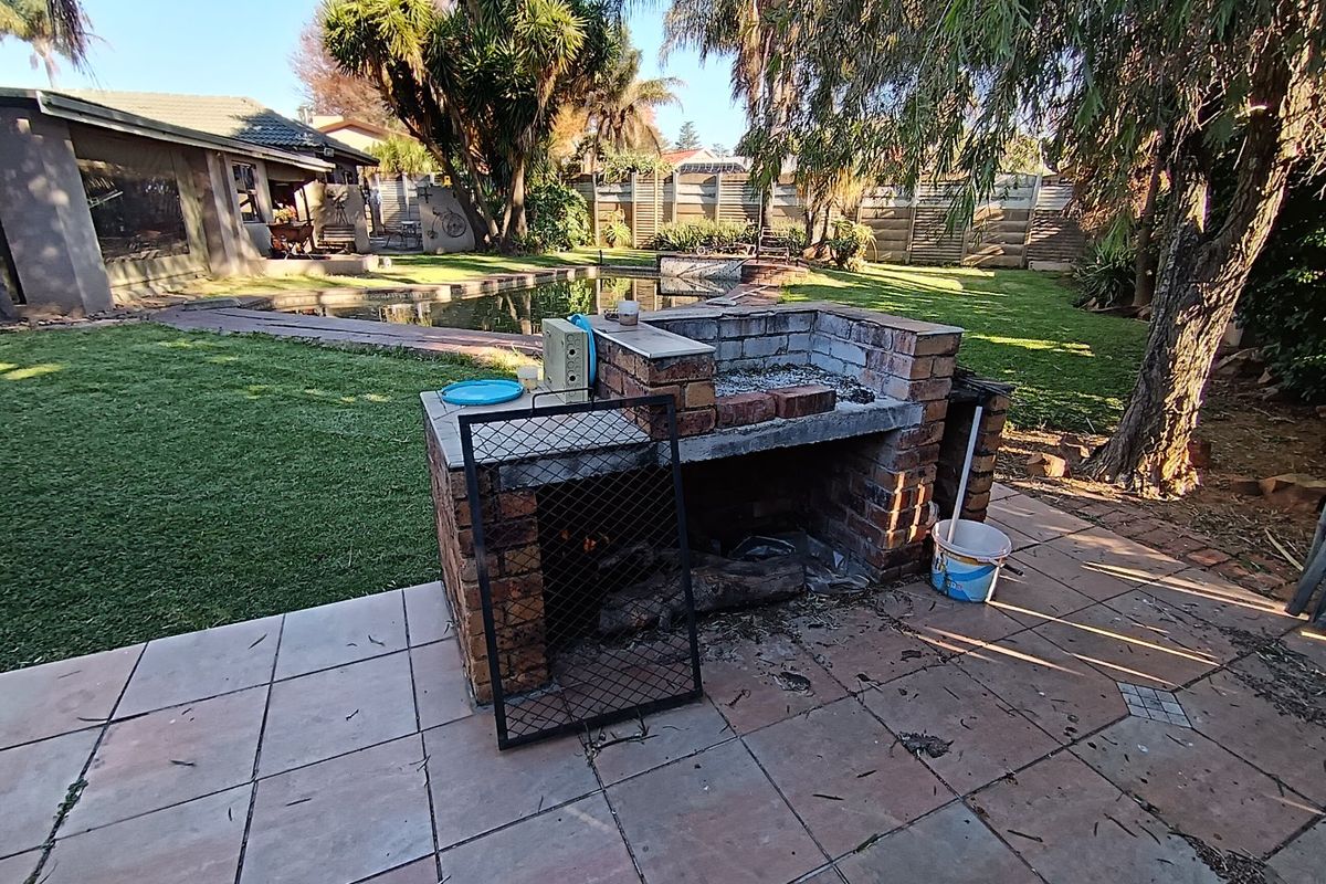 Rear garden featuring a built-in brick braai, tiled patio area, and a swimming pool set within a landscaped backyard.