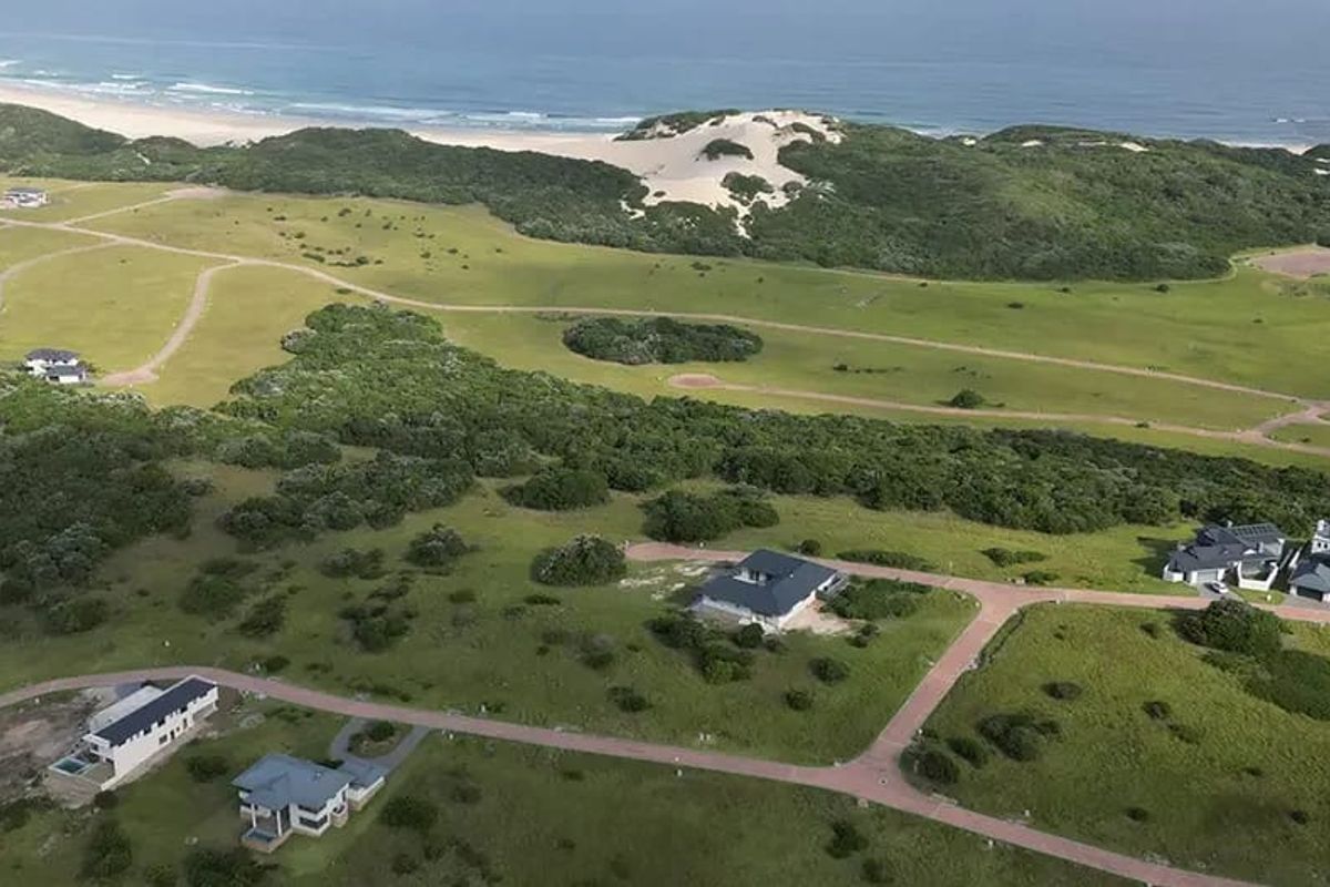 An aerial view of a coastal residential estate featuring paved roads and multiple detached houses set within a natural landscape near the beach.