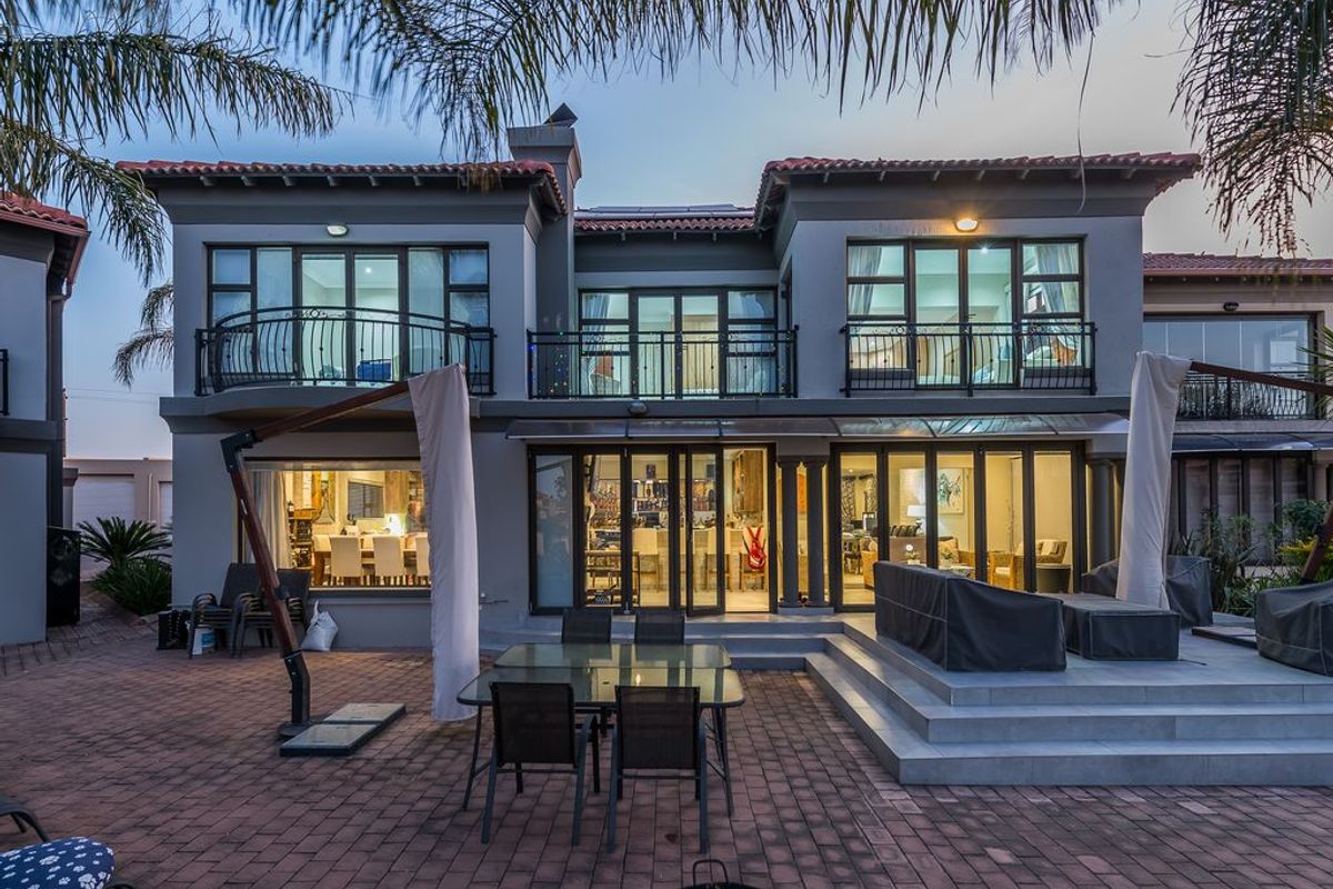 Rear elevation of a two-story residence featuring a paved patio, raised tiled terrace, and multiple folding glass doors leading to the interior living spaces.
