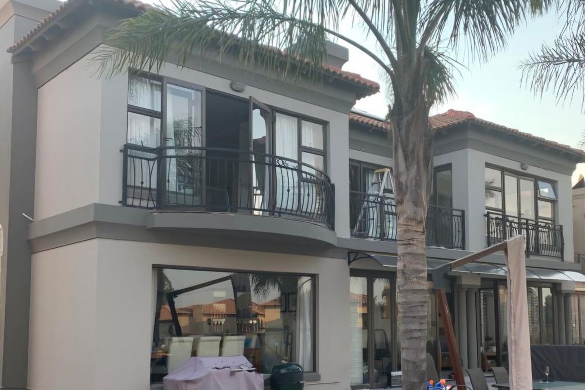 Rear elevation of a two-story house featuring upper-level balconies with wrought iron railings, large sliding doors, and a paved patio area.
