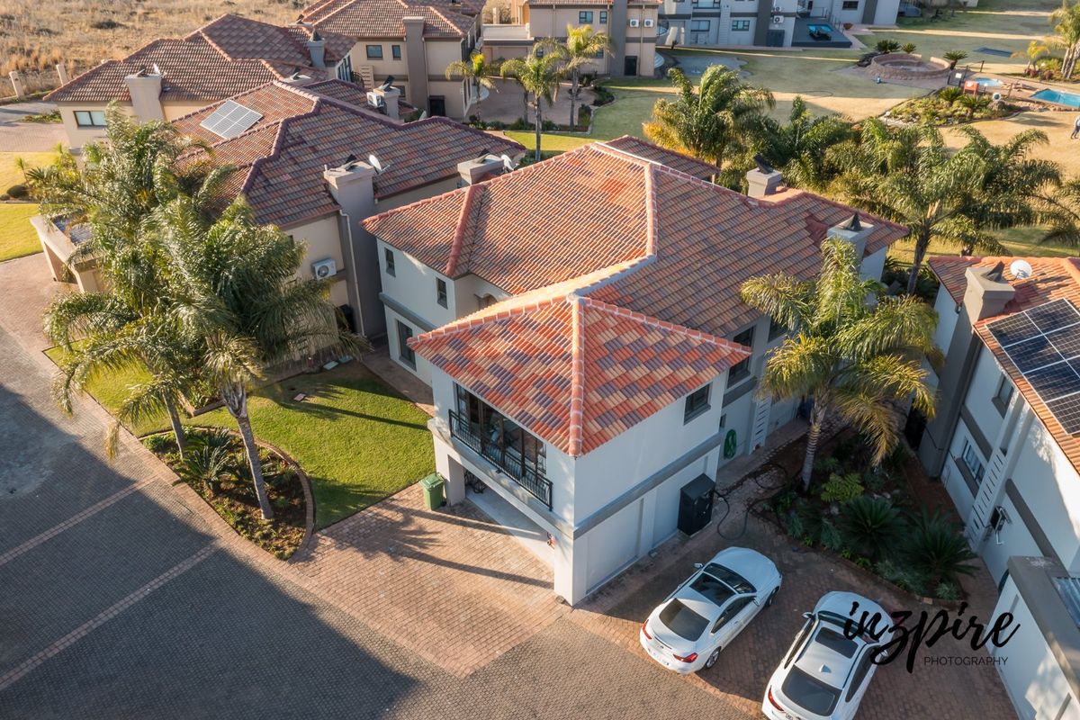 Aerial view of a residential property featuring a terracotta tiled roof, solar panels, a paved driveway, and a landscaped garden area.