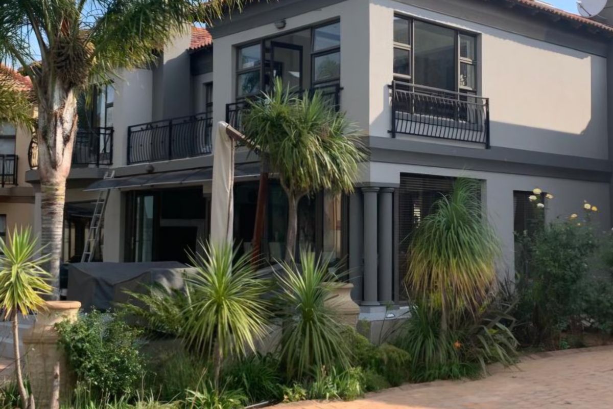 A well-maintained double-story residential property featuring a paved driveway, landscaped garden, and upper-level balconies with wrought iron railings.