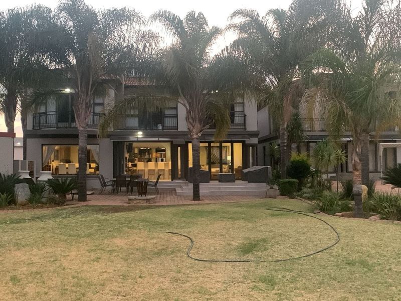 Rear view of the property featuring a paved patio area, landscaped garden with mature palm trees, and upper-level balconies.