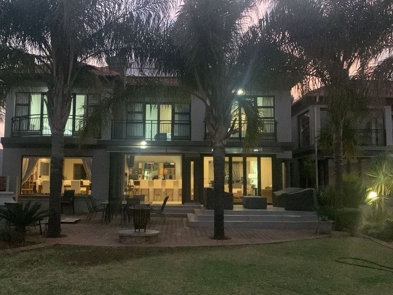 Rear view of a two-story house featuring a paved patio, balcony, and landscaped garden at dusk.