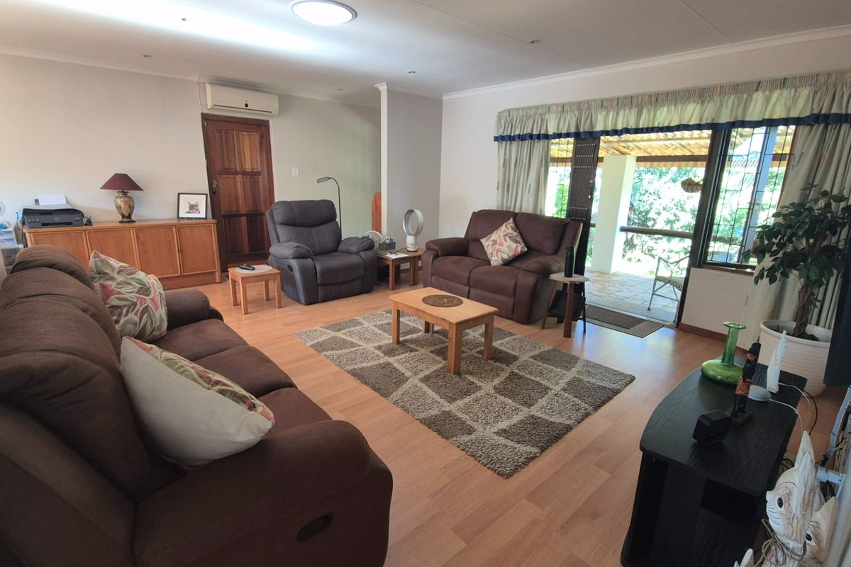 Spacious living room featuring laminate flooring, a split-system air conditioner, and large sliding glass doors providing access to an outdoor patio area.