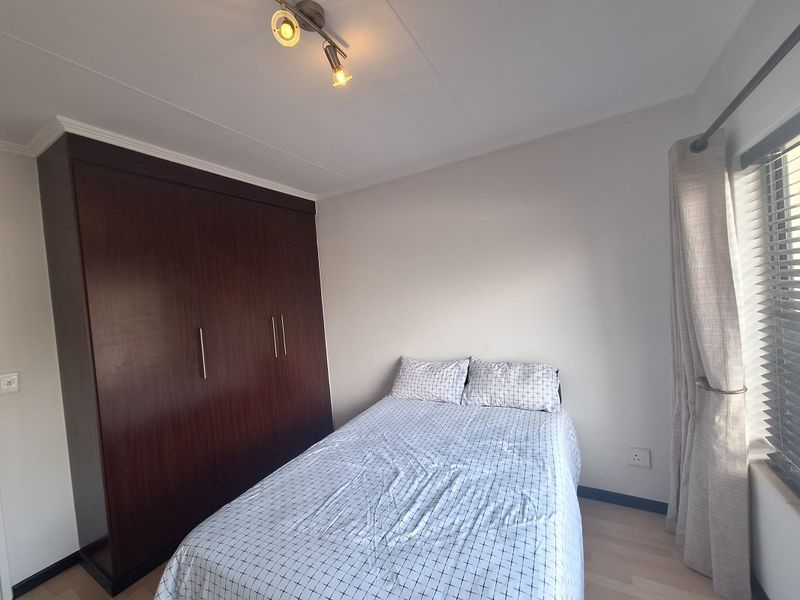 A well-maintained bedroom featuring laminate flooring, a large dark wood built-in wardrobe, and adjustable venetian blinds for natural light control.