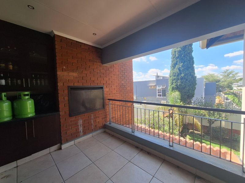 Covered balcony featuring a built-in braai, tiled flooring, and a metal balustrade, offering an outdoor entertainment space with garden views.