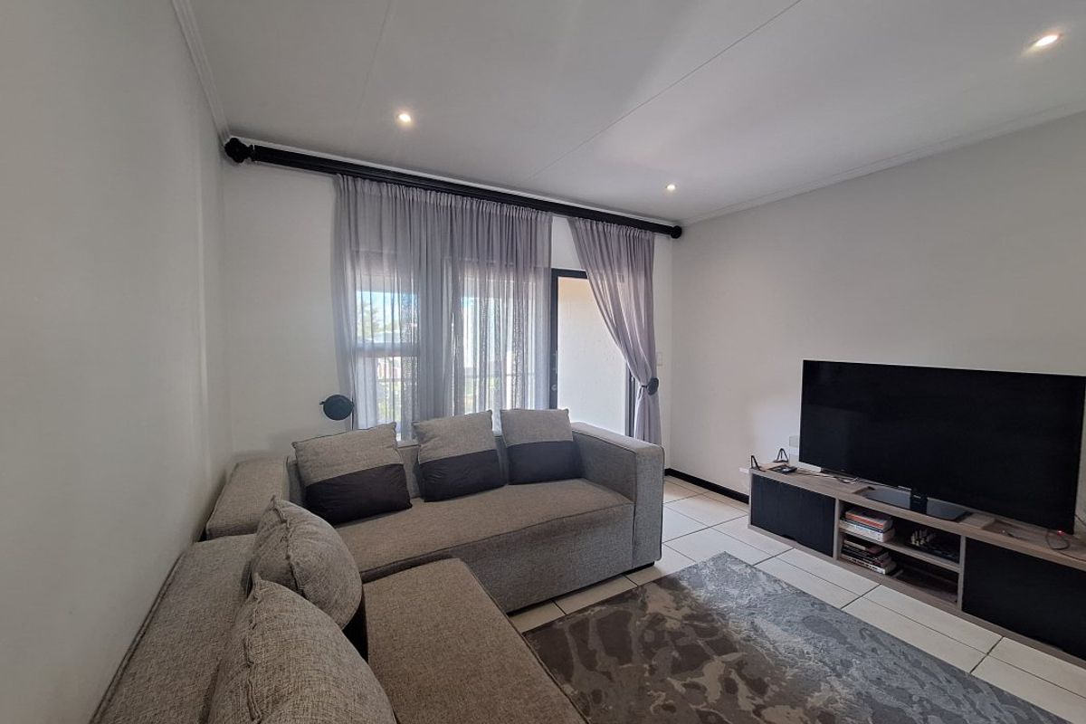 A bright living room featuring neutral tiled flooring, recessed downlighting, and a sliding glass door providing access to an outdoor area.
