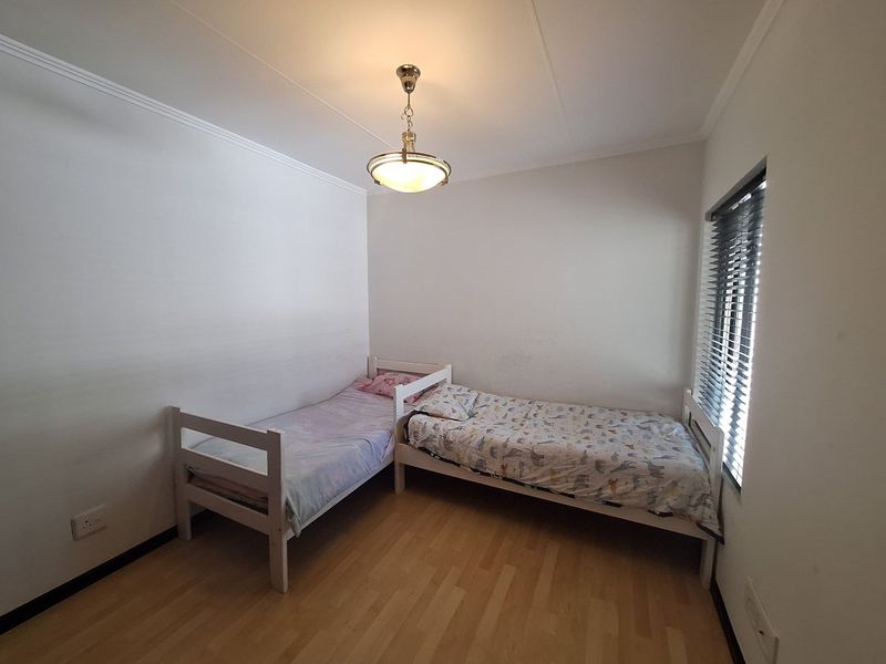 A functional bedroom featuring laminate flooring, a pendant light fixture, and venetian blinds, providing a neutral space ready for personalization.