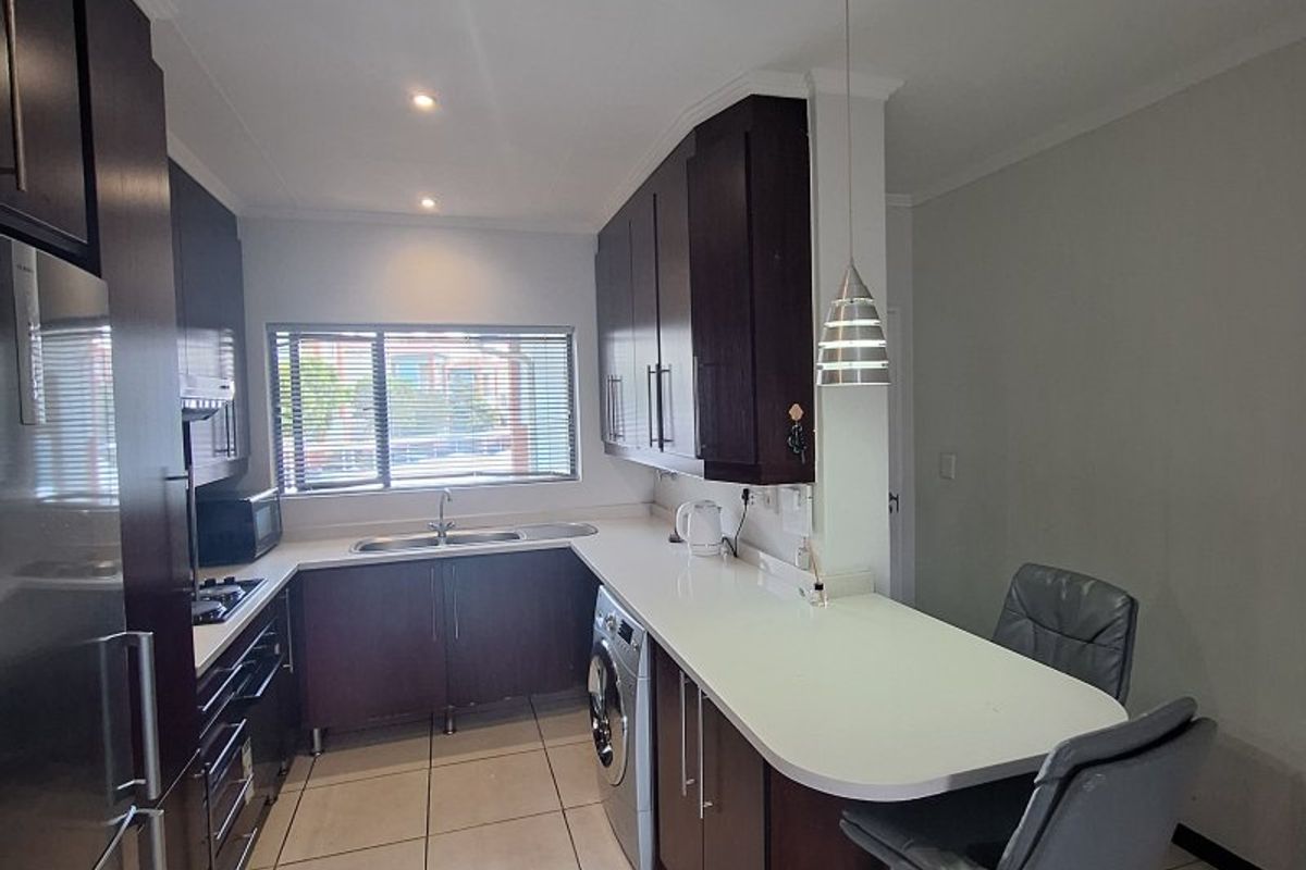 Modern kitchen featuring dark wood cabinetry, white stone countertops, integrated appliances, and a convenient breakfast bar with tiled flooring.
