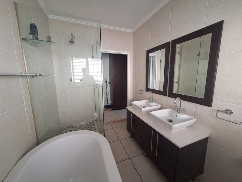 Modern bathroom featuring a double vanity with dark cabinetry, a freestanding bathtub, and a separate glass-enclosed shower with neutral wall and floor tiling.