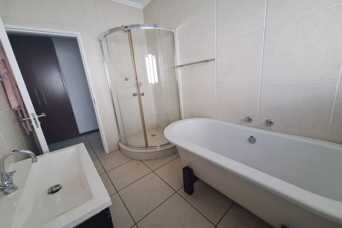 A functional bathroom featuring a freestanding bathtub, a corner shower enclosure, and a vanity basin with neutral wall and floor tiling.